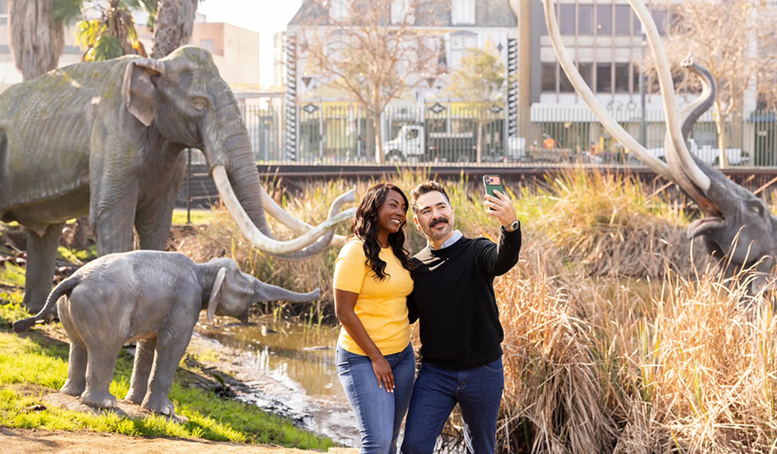 Couple holding up a camera to take a photo of themselves in front of mammoth sculptures