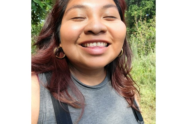 headshot image of smiling young woman wearing a grey shirt and dark red hair