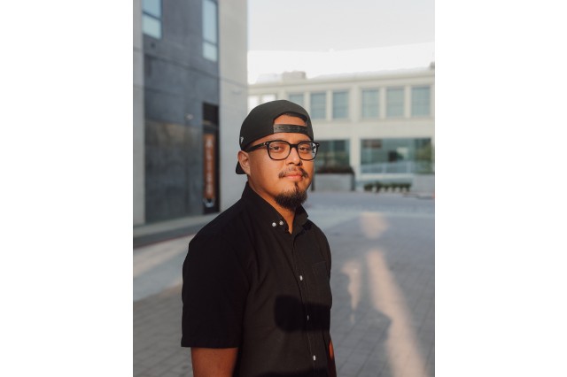 DJ Deadloop wearing a black baseball hat backwards, black glasses, and black button down short-sleeve shirt