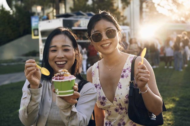 A visitor holding a cup of ice cream with another visiting wearing sunglasses and holding up a spoon