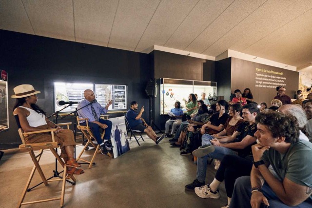 Two lecturers in high folding chairs facing an audience in chairs
