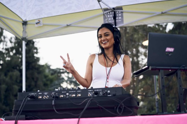 DJ standing behind sound equipment and a computer and making a peace sign