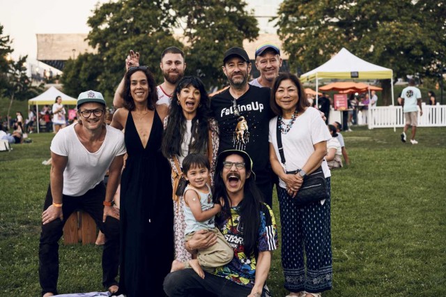 Group of visitors with arms around each other outside on the grass, with a tent in the backgroud