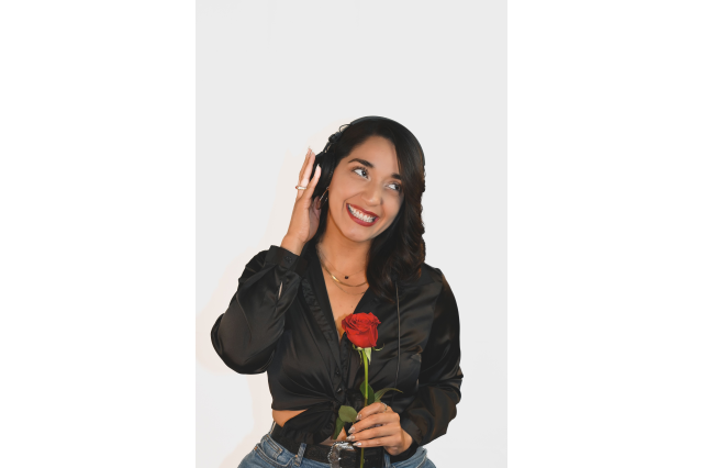 DJ ZULY wearing a black button down ties at the waist, with one hand help up to her ear and the other holding a rose