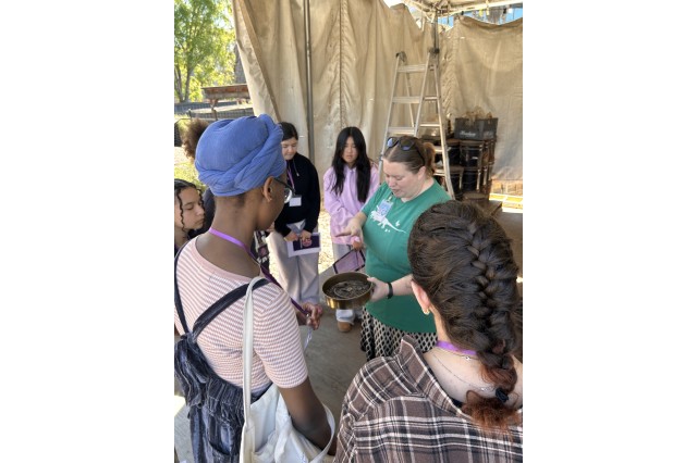 Teens gathered around Laura Tewksbury, holding up a circular tray of fossils