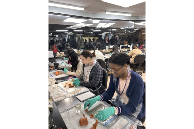 Students wearing green gloves working with terracotta pot pieces