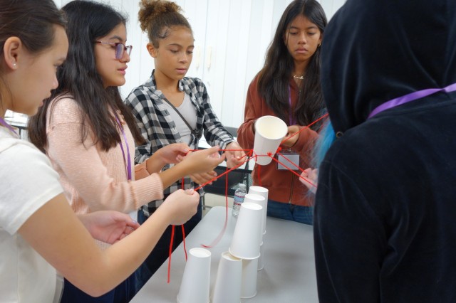 Students holding red strings suspending a cup in the air