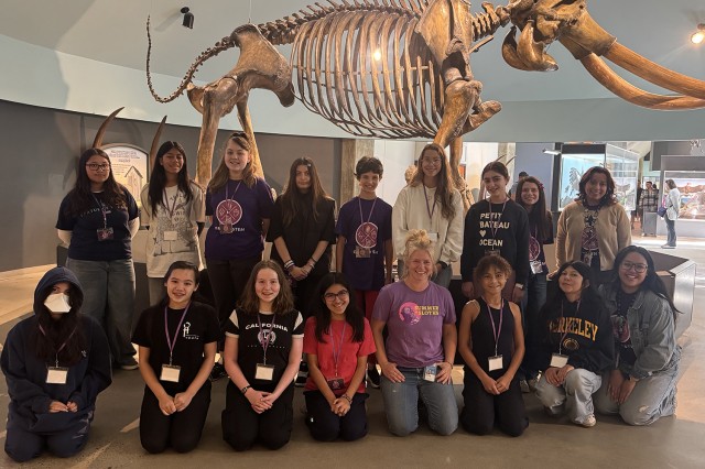 Group of students kneeling and standing in front of mammoth skeleton