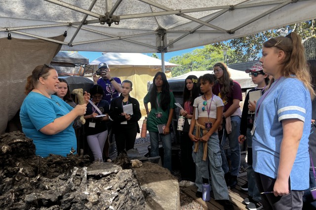 Students standing around a fossil preparator holding up a fossil specimen