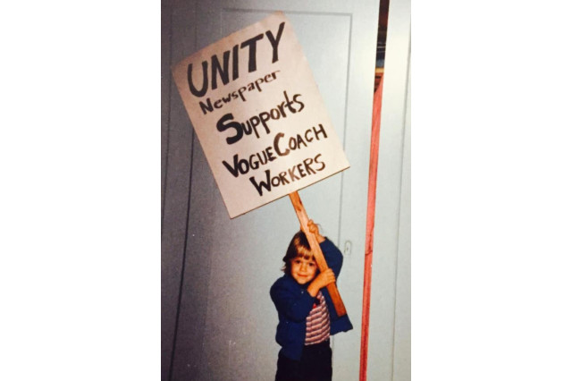 Two-year old child proudly holding a protest sign that reads "Unity newspaper supports Vogue Coach workers"
