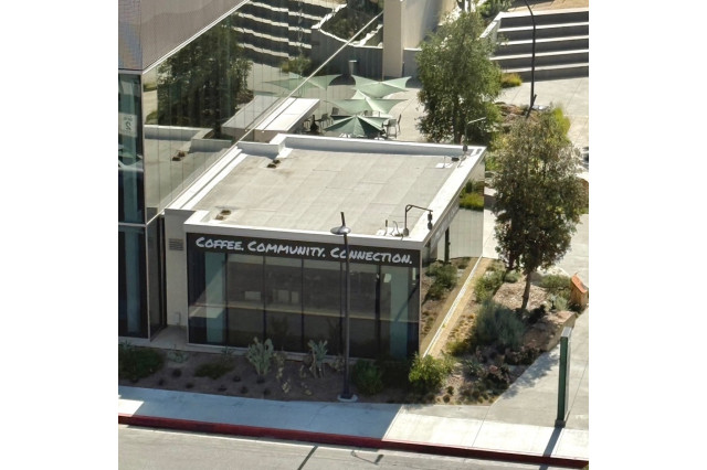 Aerial view of a glass-walled coffee shop connected to a museum with the sign "Coffee, Community, Connection" above the windows.