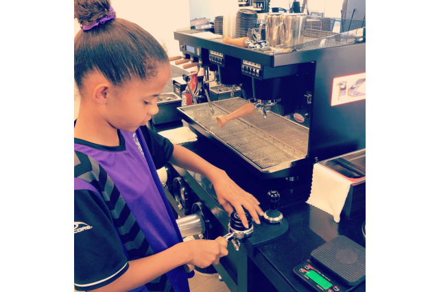 Young girl preparing coffee grounds in front of an espresso machine.