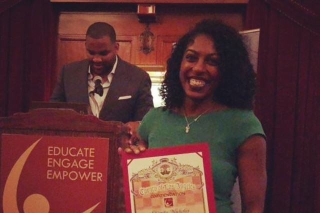 a Black woman in a green dress stands holding an award the give commendations from the County of Los Angeles to Shanita Nicolas