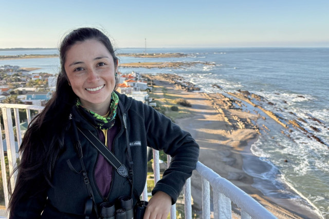 Juliana Soto-Patiño leaning on a railing with an ocean shoreline in the background