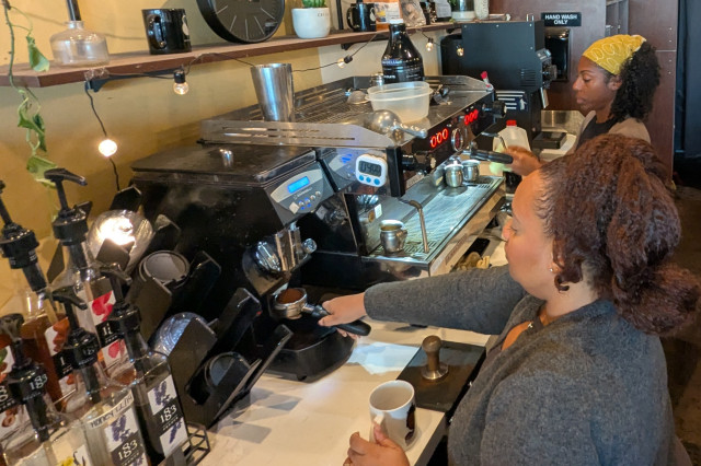 A woman pulls an espresso shot from an espresso machine as she prepares drinks in a coffee bar.