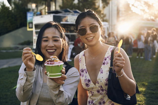 Two women facing the camera and smiling while holding up a cup of ice cream