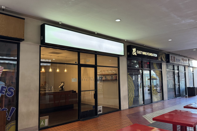 Glass-walled exterior of a bare-bones coffee shop in a non-descript shopping center interior.