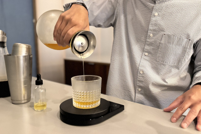 Barista pouring citrus juice into to a specialty cup of coffee.
