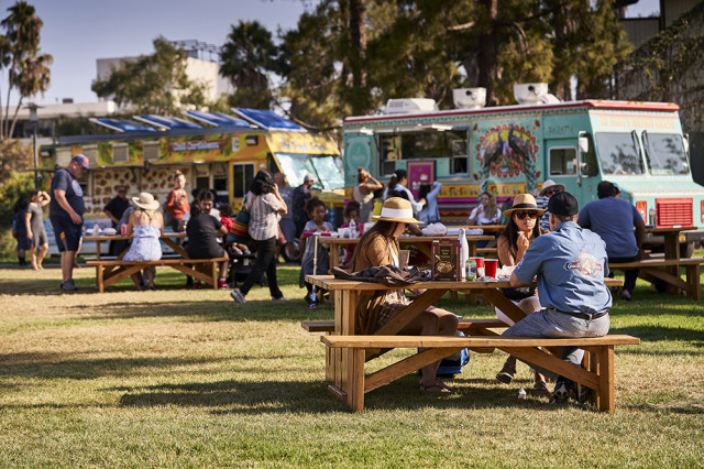 Visitor sitting at a picnic table with food trucks behind them