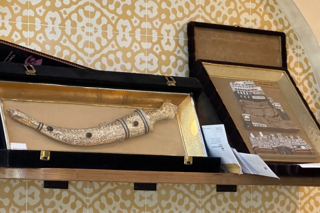 A display at Sana’a Cafe shows a traditional Yemeni jambiya dagger in a case alongside artwork of historic Sana’a architecture, highlighting cultural heritage and design.
