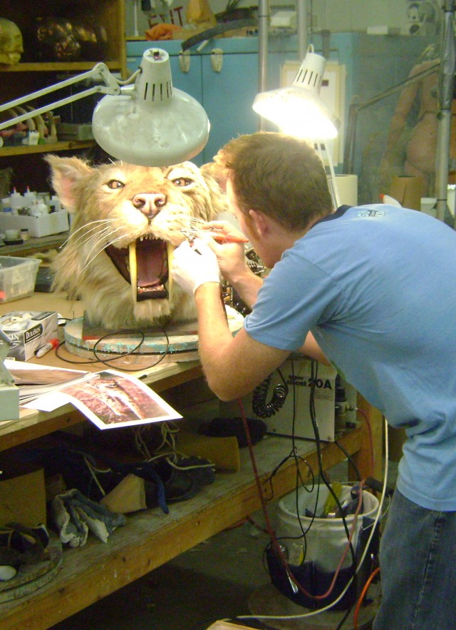 Craftsman making repairs to head of smilodon puppet