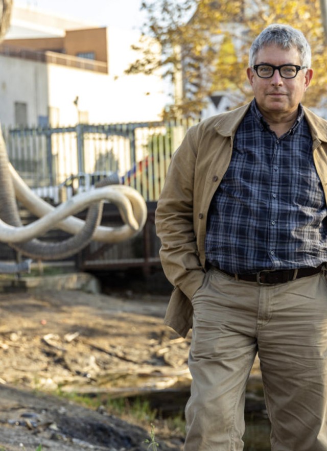 Mark Dion standing outside in front of mammoth sculptures and lake pit