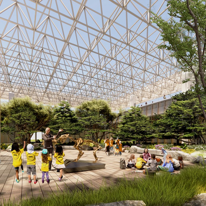 Children in yellow shirts facing a Museum Educator gesturing towards a saber-toothed cat skeleton in an outside courtyard