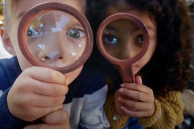 A close-up of two children holding magnifying glasses up to their face 