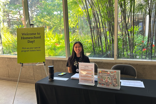 Staff member at Homeschool Day welcome table with signs and maps.
