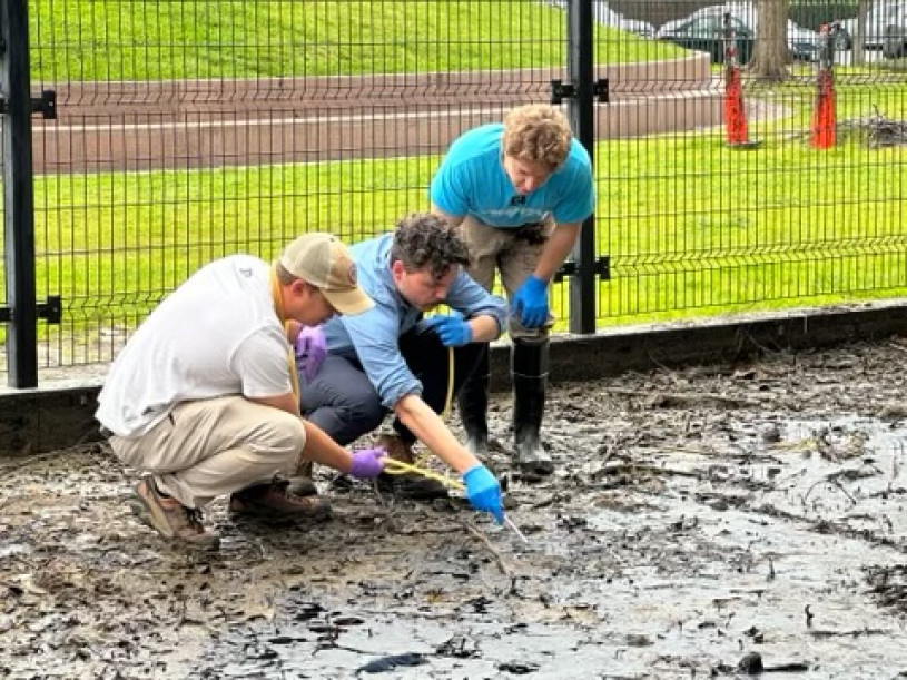Three men wearing blue gloves crouch over wet asphalt 
